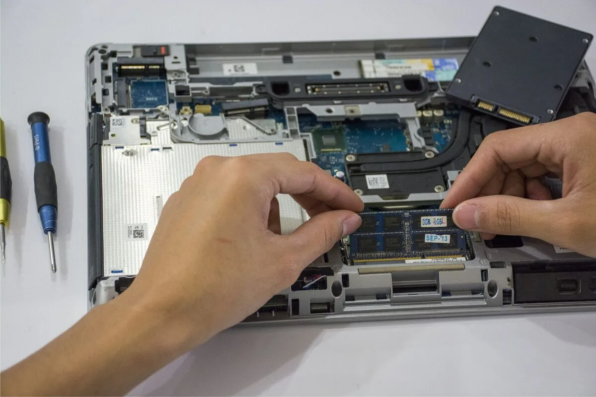 Dłonie montujące pamięć RAM obok dysku SSD wewnątrz laptopa
